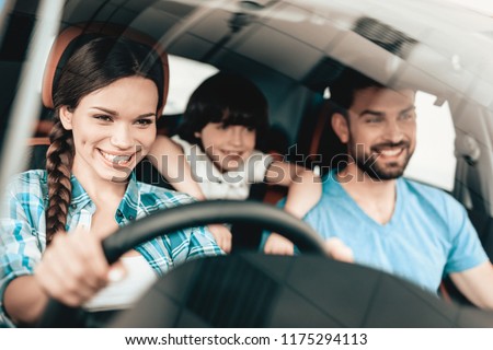 A Woman Is Sitting At The Wheel Of A New Vehicle. Smiling Family. Car Buying In A Showroom. Automobile Salon. Cheerful Driver. Happy Together. Successful Buying. Good Mood. Great Trade.