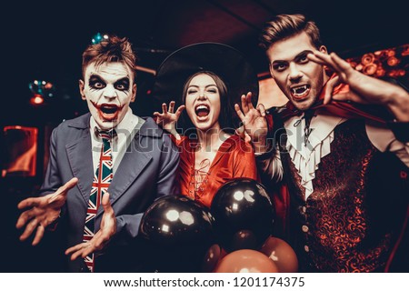 Young People in Costumes Celebrating Halloween. Group of Young Happy Friends Wearing Halloween Costumes having Fun at Party in Nightclub by doing Scary faces. Celebration of Halloween