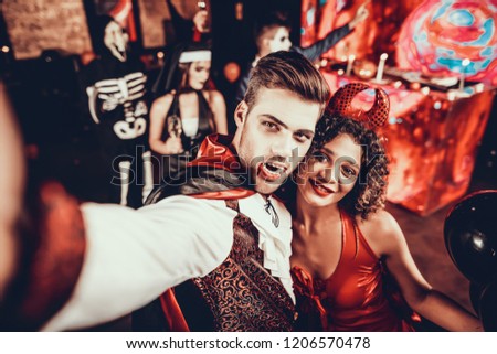 Young Couple in Halloween Costumes taking Selfie. Beautiful Woman and Handsome Young Man Wearing Costumes having Fun at Halloween Party in Nightclub. Happy Friends having Fun Celebrating Halloween