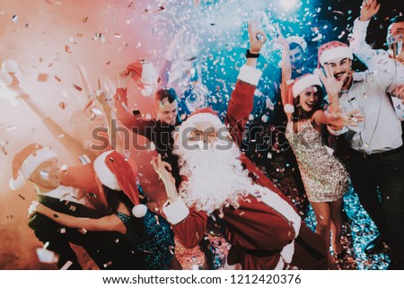 Man in Santa Claus Costume on New Year Party. Happy New Year. People Have Fun. Indoor Party. Celebrating of New Year. Young Women in Dresses. Young Men in Suits. Happy People. Man with White Beard.