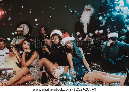 Three Young Women Celebrating New Year on Party. Santa Claus Cap. People in Red Caps. Happy New Year Concept. Glass of Champagne. Celebrating of New Year Concept. Young Woman in Dress.