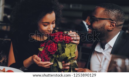 African American Couple Dating in Restaurant. Romantic Couple in Love Dating. Cutel Man and Girl in a Restaurant Making Order. Romantic Concept. Man Giving Bouquet of Flowers. Red Roses.