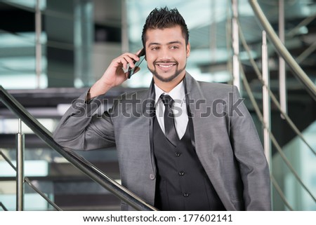 Young Asian Indian businessman standing on office background and talking on the phone