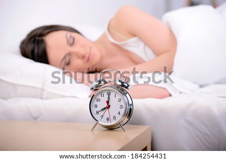 Young beautiful woman sleeping on bed with alarm clock in bedroom