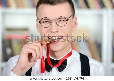 Smart young man intelligent in shirt and tie tie and glasses, standing holding a medal in a library