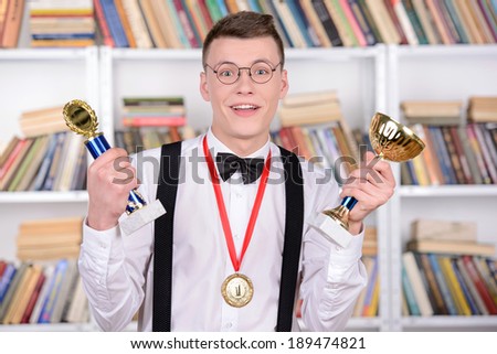 Smart young man intelligent in shirt and tie tie and glasses holding a medal and cup champion standing in the library