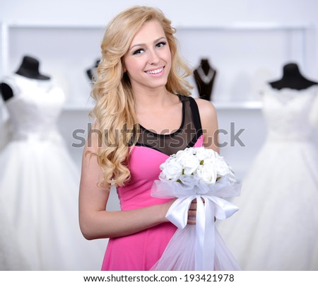 Smiling pretty bride chooses white gown at shop of wedding fashion