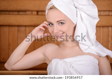 Beautiful woman in sauna. Attractive young woman wrapped in towel relaxing in sauna and smiling to you