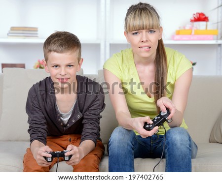 A beautiful woman and her teenage son at home, sitting on a couch playing a video game.
