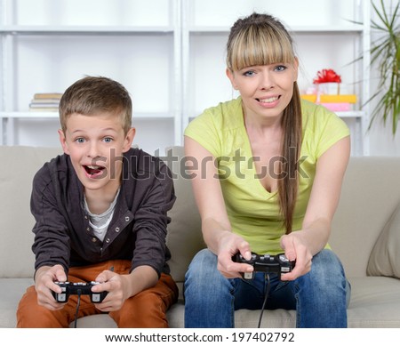 A beautiful woman and her teenage son at home, sitting on a couch playing a video game.