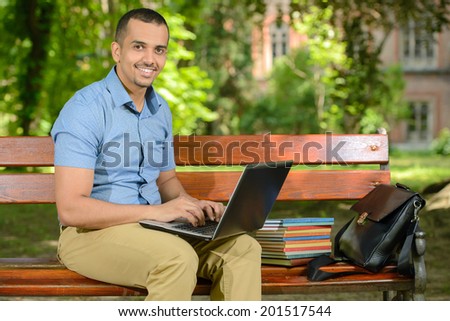 Young male student learning using laptop outdoors in the park