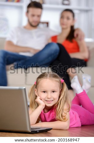 Little girl using a laptop on the background of the parents to watch TV