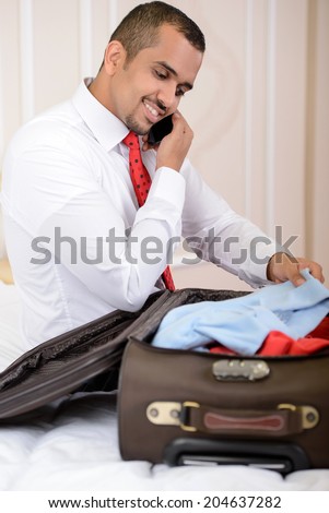 Portrait of Asian businessman with a suitcase, sitting on the bed and makes things up a suitcase in hotel room