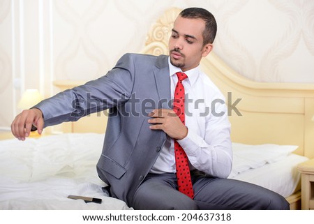 Portrait of Asian businessman with a suitcase sitting on the bed and wear a jacket in the hotel room