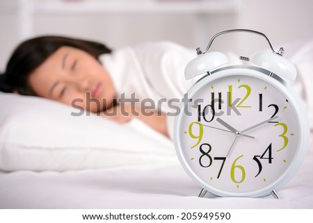 Sleep. Portrait of Asian woman sleeping on the bed at home. Great alarm clock in the foreground