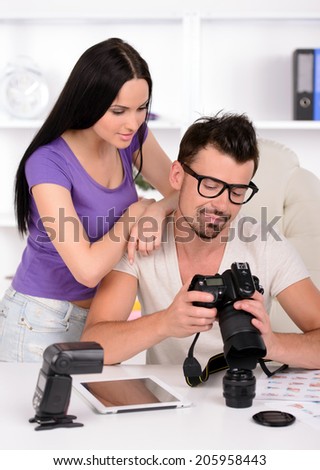 Photographer is looking at photo on camera. Girl is standing behind and looking at camera as well.