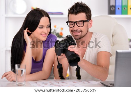 Photographer is looking at photo on camera. Girl is standing behind and looking at camera as well.