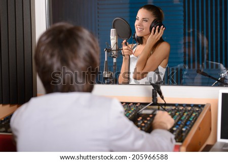 Young female singer with studio technician in foreground at the recording studio