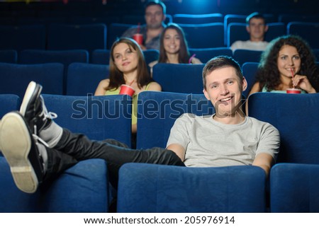 Watching a movie. Young men holding his feet on the seat while watching movie at cinema