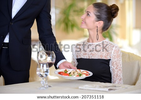 Young elegant man waiter serve wine for a young elegant woman in a restaurant