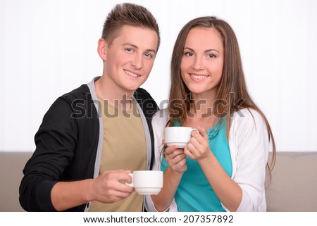 Young emotional couple drinking tea or coffee while sitting on sofa at home