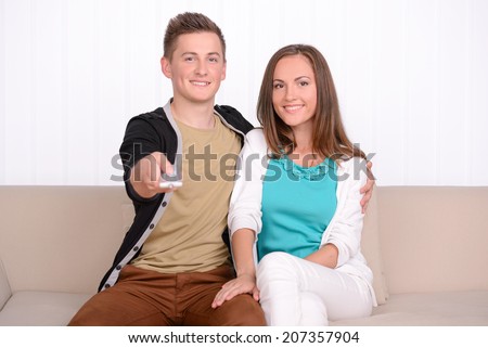 Young emotional couple watching TV, sitting on the sofa at home