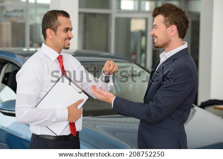 Giving a key of a brand new car. Handsome young classic car salesman giving a car key to the owner and smiling