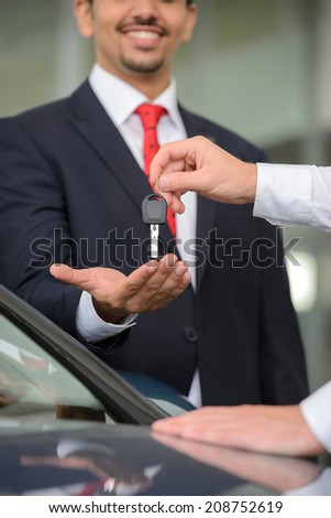 Giving a key of a brand new car. Handsome young classic car salesman giving a car key to the owner and smiling