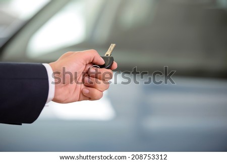 Close up shoot of the hand holding car keys in front of a car