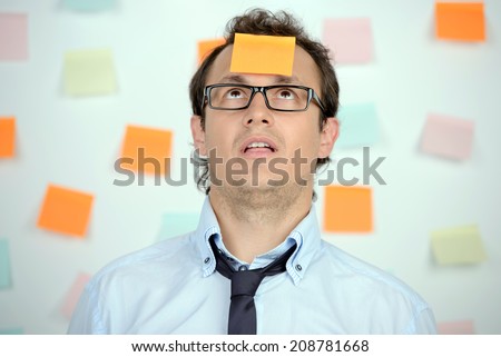 Portrait of frustrated young man in formalwear and adhesive note on his forehead standing against the wall with many adhesive notes on it