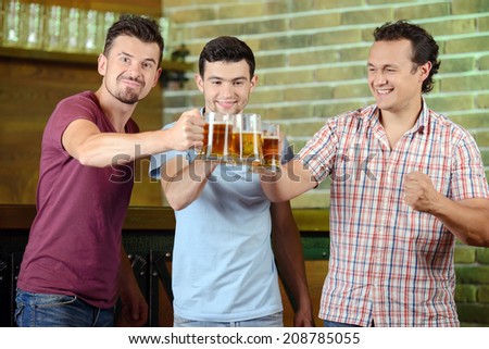 Friends cheering. Three happy soccer fans drinking beer at the pub