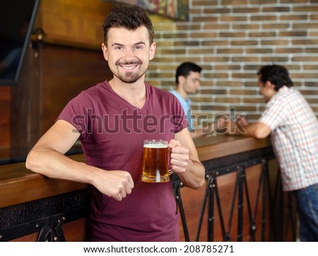 Man in bar. Handsome young man drinking beer in bar and smiling