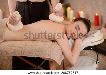 Smiling woman getting a back massage with herbal compresses in the health spa