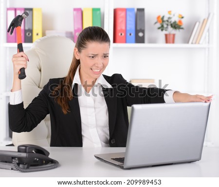 Freaked out businesswoman with a hammer ready to smash her laptop computer