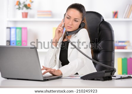 Talking at phone. Confident middle-aged businesswoman sitting at her working place and looking over shoulder