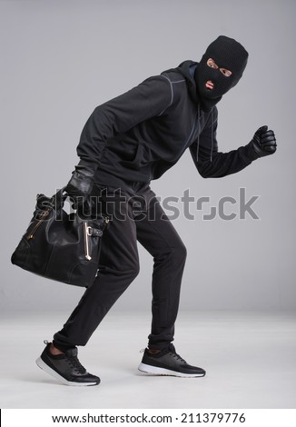Portrait of running male burglar with a handbag. Isolated on gray background