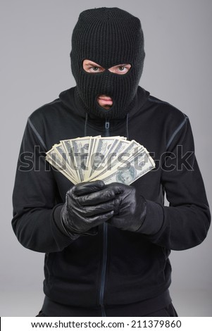 Robber in a mask rejoice stolen money. Gray background