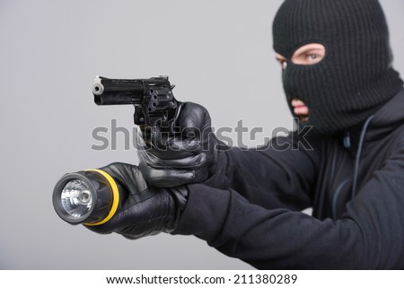 Masked robber with gun aiming into the camera against a black background