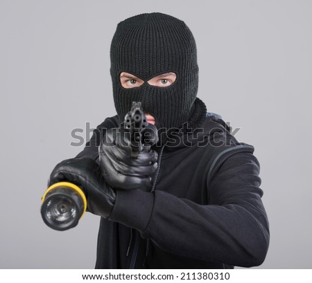 Masked robber with gun aiming into the camera