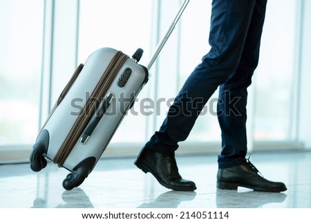 Business traveler pulling suitcase and holding passport and airline ticket