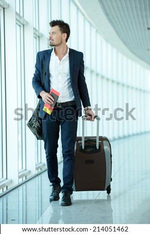 Business traveler pulling suitcase and holding passport and airline ticket