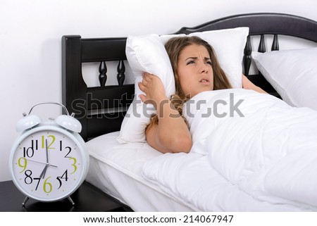 Young angry girl who woke up very early to call an alarm clock in the bedroom