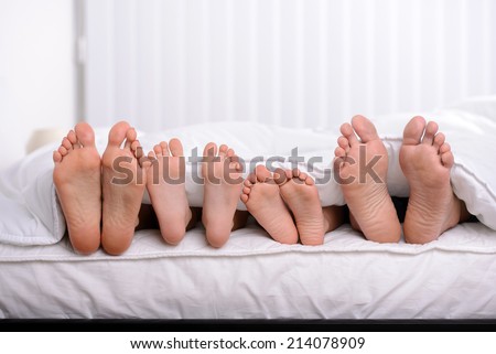 Mother, father and two children lie on bed with white sheets; focus on feet