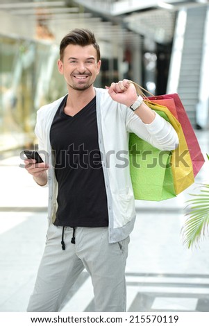 Shopping. Young handsome man with bags for shopping talking on the phone in a shopping center