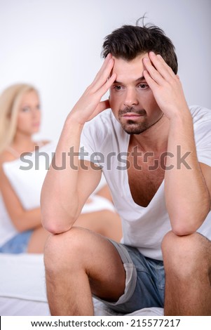 Problems in the family. Young is confident man sitting on the bed, against his angry wife