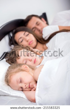 Family in the bedroom. Young family. Dad, mom, little boy and little girl sleeping in bed in bedroom at home