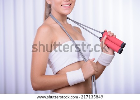 Laughing sporty brunette wearing a skipping rope around the neck in bright room