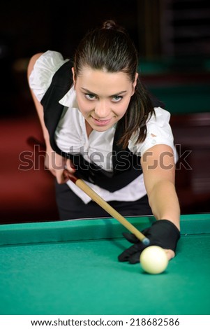 Young woman playing billiards in the dark billiard club