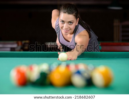 Young woman playing billiards in the dark billiard club