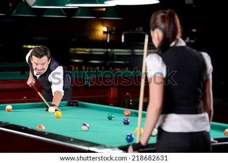 Young man and woman playing professional billiards in the dark billiard club